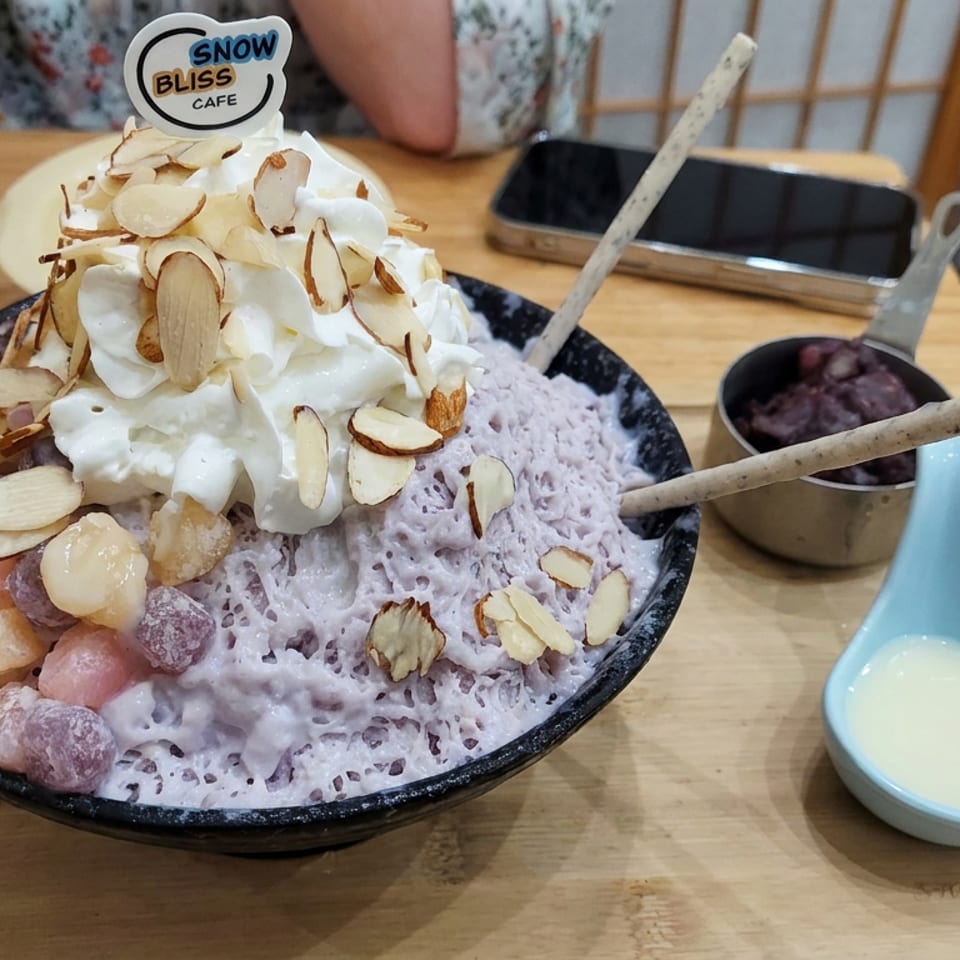 Lavender shaved ice topped with whipped cream, sliced almonds, and colorful fruit pieces at Snow Bliss Cafe.