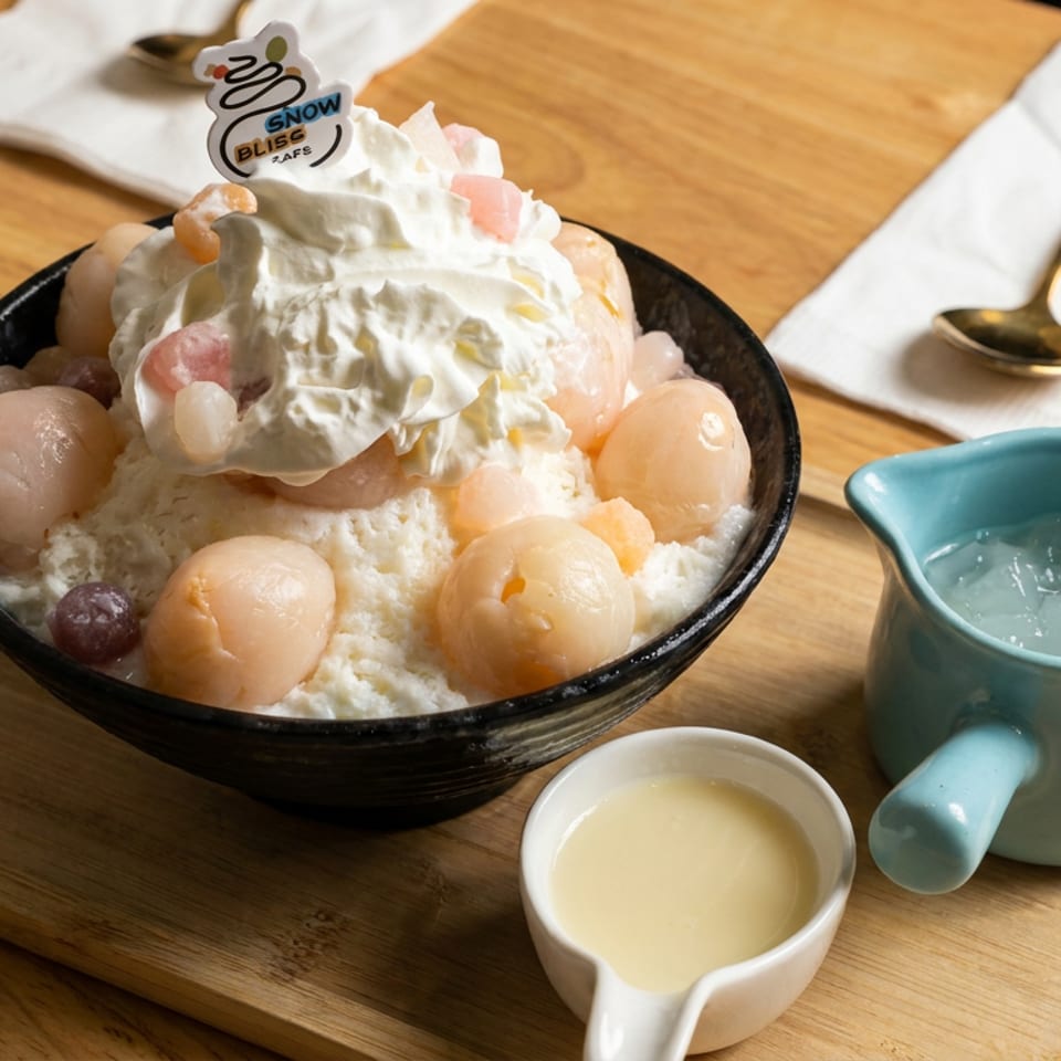 Shaved ice dessert topped with whipped cream, lychees, and fruit, served in a black bowl with sauces and a blue pitcher.